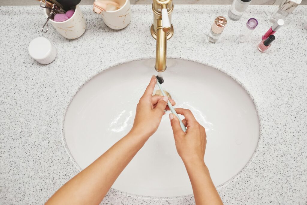 Close-up of hands cleaning a toothbrush under running water in a modern bathroom.